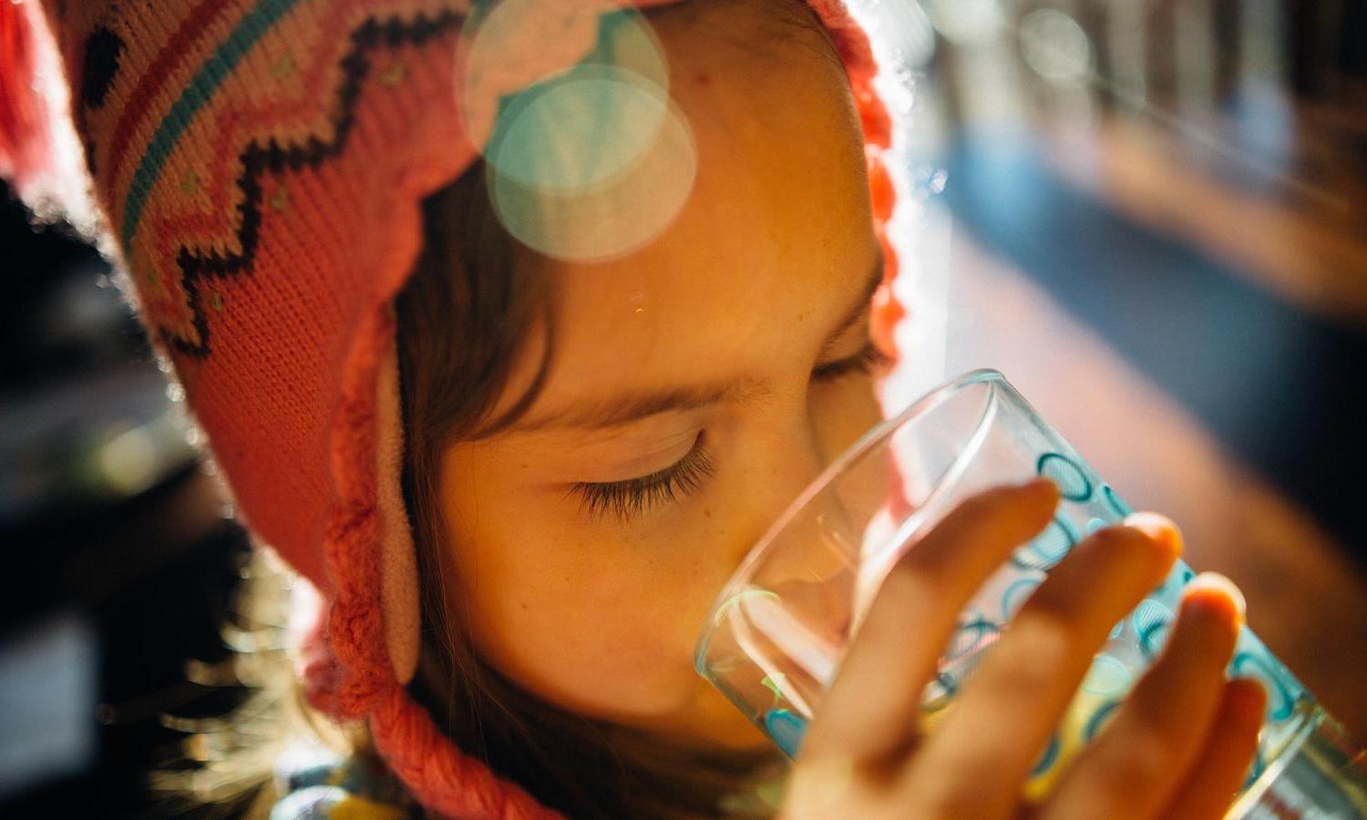 A kid drinks a glass of water.